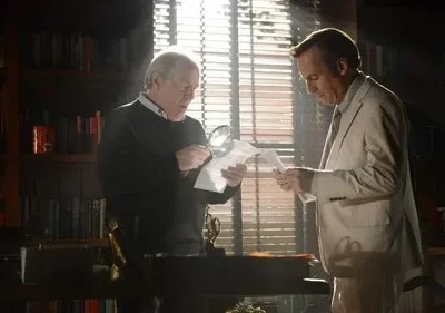 Em um escritório, um homem de suéter usa lupa para examinar papéis com outro de terno claro. Estantes e luz intensa pela janela criam clima sério.