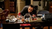 Um homem de camiseta escura inclinado sobre uma mesa, olhando aquários e um equipamento de laboratório improvisado.