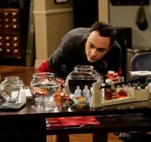 Um homem de camiseta escura inclinado sobre uma mesa, olhando aquários e um equipamento de laboratório improvisado.