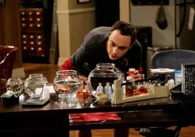 Um homem de camiseta escura inclinado sobre uma mesa, olhando aquários e um equipamento de laboratório improvisado.