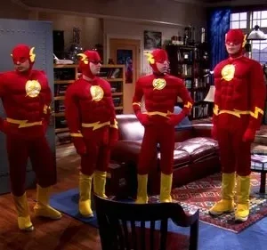 Quatro homens em trajes de super-herói vermelhos com detalhes amarelos e máscaras posam em uma sala de estar. Clima humorístico.