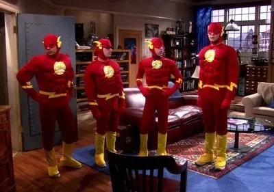 Quatro homens em trajes de super-herói vermelhos com detalhes amarelos e máscaras posam em uma sala de estar. Clima humorístico.