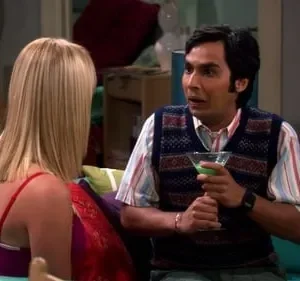 Homem de colete e camisa listrada, segurando um drink verde, olha surpreso para mulher loira de costas. Sala colorida.