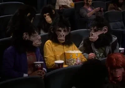 Várias pessoas usando máscaras realistas de macaco e cabelo falso assistem a um filme em um cinema escuro, comendo pipoca. Clima divertido.