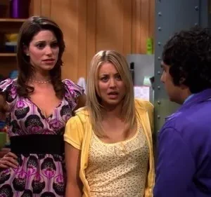 Duas mulheres com expressões de surpresa/choque encaram um homem de casaco roxo, visto de costas, em uma sala.