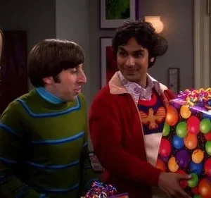 Um homem sorridente oferece um presente colorido de balões. Outro homem de verde e uma mulher loira conversam.