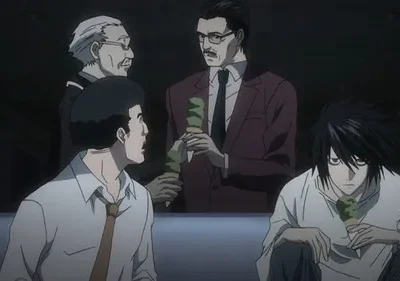 Quatro homens em sala escura. Um jovem de cabelo preto bagunçado está curvado com sorvete. Outros três conversam, alguns também com sorvete. Ambiente sério.