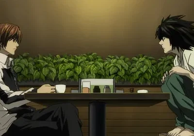 Dois personagens de anime se encaram em uma mesa de café com folhagem verde. Um sentado, outro agachado.