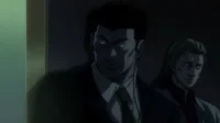 Dois homens sérios em ternos, um com olhar intenso e earpiece no escuro, o outro atrás. Clima tenso e misterioso.
