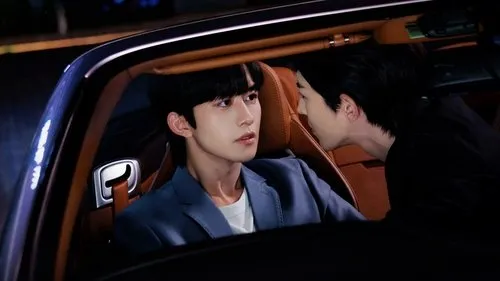 Dois homens jovens em um carro à noite. Um no banco do motorista; o outro se inclina perto dele, criando um clima íntimo e tenso.