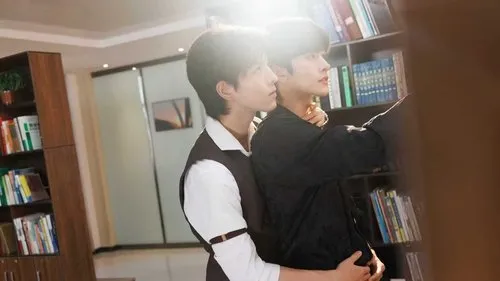 Dois jovens se abraçam em uma biblioteca iluminada. Um estende a mão para um livro. A cena tem um clima romântico e sereno.