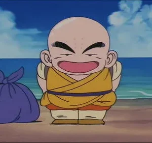 Pequeno monge careca de gi amarelo e pontos na testa sorri feliz numa praia ensolarada. Uma trouxa roxa ao lado, com mar azul e céu claro.