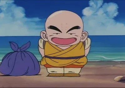 Pequeno monge careca de gi amarelo e pontos na testa sorri feliz numa praia ensolarada. Uma trouxa roxa ao lado, com mar azul e céu claro.