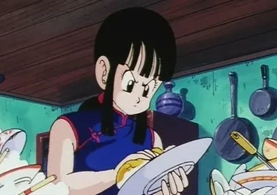 Mulher de cabelo preto em vestido azul lava uma pilha enorme de louça suja em uma cozinha verde. Sua expressão é de aborrecimento.