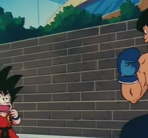 Pequeno lutador com cauda e homem musculoso de luvas de boxe se encaram. Fundo de parede de tijolos e céu azul. Clima de luta animada.