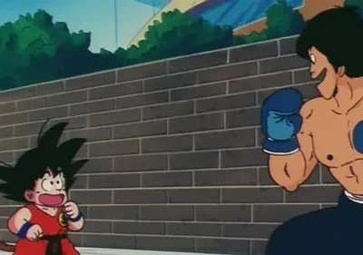 Pequeno lutador com cauda e homem musculoso de luvas de boxe se encaram. Fundo de parede de tijolos e céu azul. Clima de luta animada.