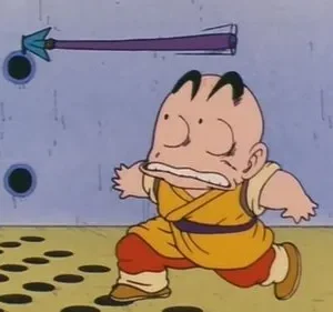 Um personagem careca de gi amarelo corre aterrorizado. Uma flecha roxa voa por uma parede azul com furos. O chão tem um padrão de círculos.