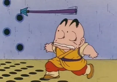 Um personagem careca de gi amarelo corre aterrorizado. Uma flecha roxa voa por uma parede azul com furos. O chão tem um padrão de círculos.