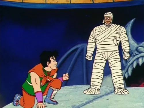 Dragon Ball – T01E72:A Luta de Goku na Piscina do Diabo 1 Homem agachado em traje de luta laranja e verde encara um oponente tipo múmia em pé. Fundo escuro com cabeça de dragão de pedra.