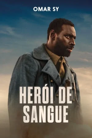 Homem negro barbudo em uniforme militar cinza, com um rifle, olha intensamente para o lado, contra um céu nublado.