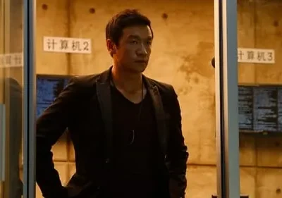 Homem asiático sério de blazer escuro em ambiente tecnológico. Monitores exibem código, criando um clima misterioso.