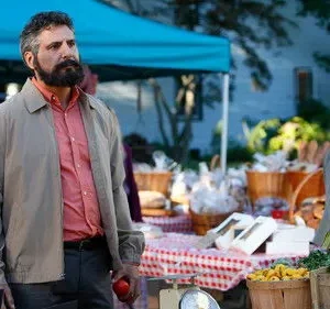 Homem barbudo e mulher em mercado ao ar livre. Barracas coloridas com produtos frescos e comida. Ele segura uma maçã.