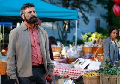 Homem barbudo e mulher em mercado ao ar livre. Barracas coloridas com produtos frescos e comida. Ele segura uma maçã.