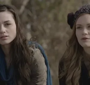 Pôster: Duas jovens ao ar livre. Uma com cabelo escuro e cachecol azul; a outra ruiva com gorro. Ambas com expressão séria e atenta.