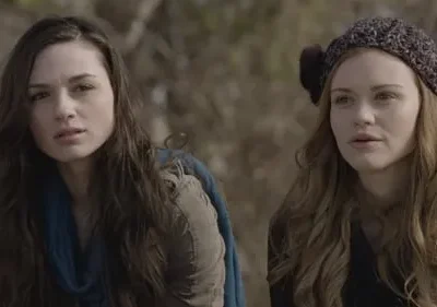 Pôster: Duas jovens ao ar livre. Uma com cabelo escuro e cachecol azul; a outra ruiva com gorro. Ambas com expressão séria e atenta.