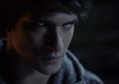 Jovem em close-up, com olhos dourados brilhantes e pupilas fendidas na escuridão. Atmosfera sobrenatural.