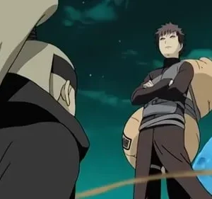 Um homem de cabelo claro e capa escura de costas. Em frente, um jovem de braços cruzados, com cabaça às costas, sob céu noturno.