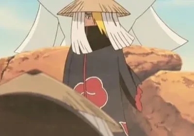 Personagem de chapéu cônico, cabelo loiro e capa preta com nuvens vermelhas em rochas. Outro chapéu no primeiro plano.