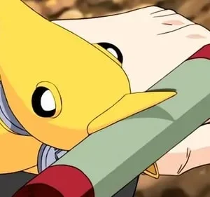 Uma criatura amarela animada com olhos grandes e focinho observa uma mão humana segurando um bastão verde e vermelho. Fundo desfocado.