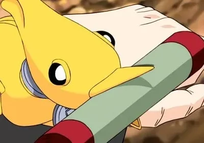 Uma criatura amarela animada com olhos grandes e focinho observa uma mão humana segurando um bastão verde e vermelho. Fundo desfocado.