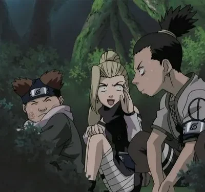 Três jovens animados em uma floresta. Um menino sorri dos arbustos, uma menina loira está chocada, e outro com rabo de cavalo parece irritado.