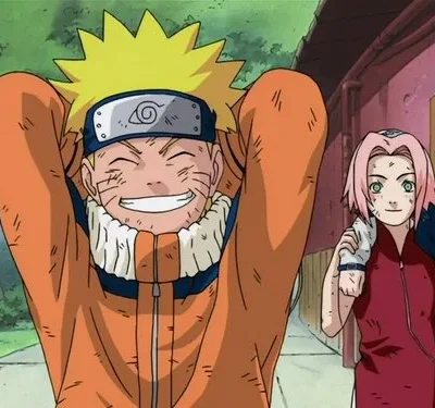 Um jovem loiro de laranja sorri feliz, mãos na cabeça, ladeado por uma garota de cabelo rosa e um garoto de cabelo escuro. Todos estão sujos, em cenário urbano.