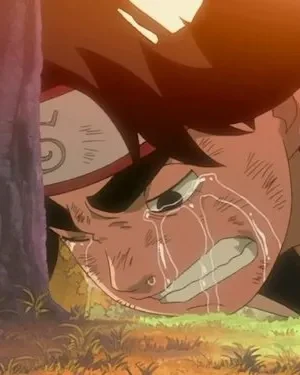 Um jovem de anime com faixa na cabeça chora em agonia no chão, rosto com arranhões. Está encostado numa árvore, sob luz quente de pôr do sol.