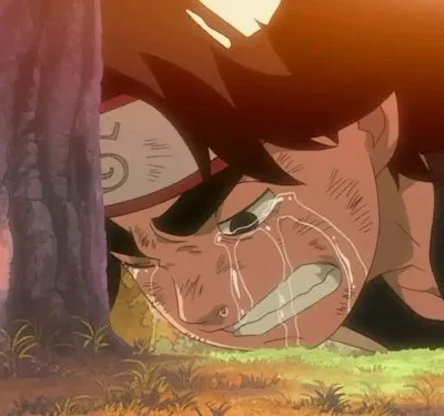 Um jovem de anime com faixa na cabeça chora em agonia no chão, rosto com arranhões. Está encostado numa árvore, sob luz quente de pôr do sol.