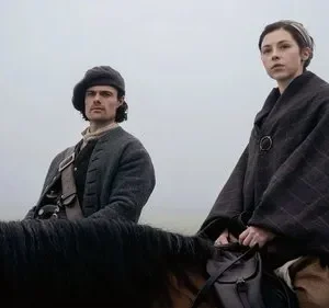 Duas figuras de época a cavalo, um homem e uma mulher, em uma paisagem cinzenta e enevoada. O clima é sério e pensativo.