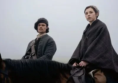 Duas figuras de época a cavalo, um homem e uma mulher, em uma paisagem cinzenta e enevoada. O clima é sério e pensativo.