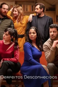 Sete adultos,4 homens e 3 mulheres,em uma reunião. Roupas coloridas,expressões sérias e pensativas. Ambiente interno com estantes de livros.