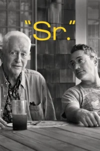 Dois homens em preto e branco à mesa. Um mais velho sorri para a câmera,enquanto um mais jovem com óculos o observa. Cena íntima e reflexiva.