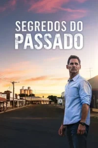 Homem pensativo de camisa azul em rua deserta de cidade rural ao pôr do sol. Silos e prédios antigos compõem o cenário.
