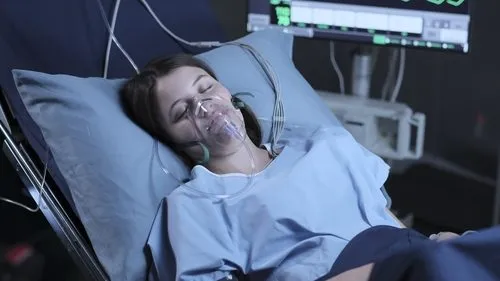 The Good Doctor:O Bom Doutor – T01E04:Encanamentos 1 Mulher deitada em leito hospitalar,olhos fechados,com máscara de oxigênio. Monitor de sinais vitais brilhando no escuro ao fundo.