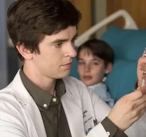 Jovem médico em jaleco branco examina um frasco, com menino paciente na cama de hospital observando-o.