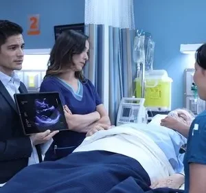 Médicos e enfermeiras cercam paciente idoso em hospital. Um médico de terno mostra exame de ultrassom em tablet, com ar sério.
