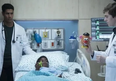 Dois médicos em um quarto de hospital interagem com uma criança doente na cama. Um segura um Sr. Cabeça de Batata para ela. Clima cuidadoso.