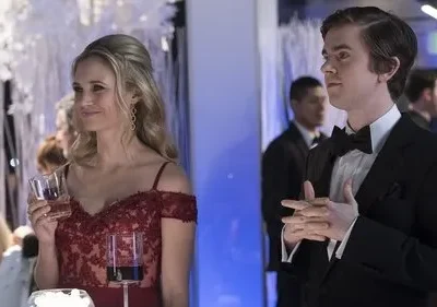 Mulher sorridente de vestido vermelho e homem de smoking em festa elegante. Decoração branca e luz azul no fundo.