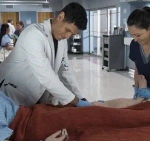 Jovem paciente em hospital, médico e enfermeira sorridente examinando sua perna. O paciente reage com a boca aberta.