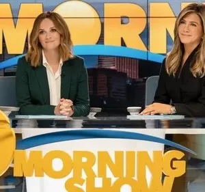 Duas apresentadoras sorridentes sentadas em uma bancada de estúdio de TV. Um painel exibe uma cidade e MORNING SHOW ao fundo.
